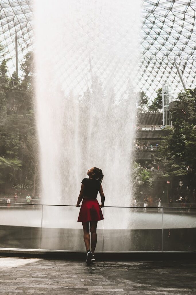 A woman admires the Jewel Changi Airport waterfall in Singapore, surrounded by lush greenery.